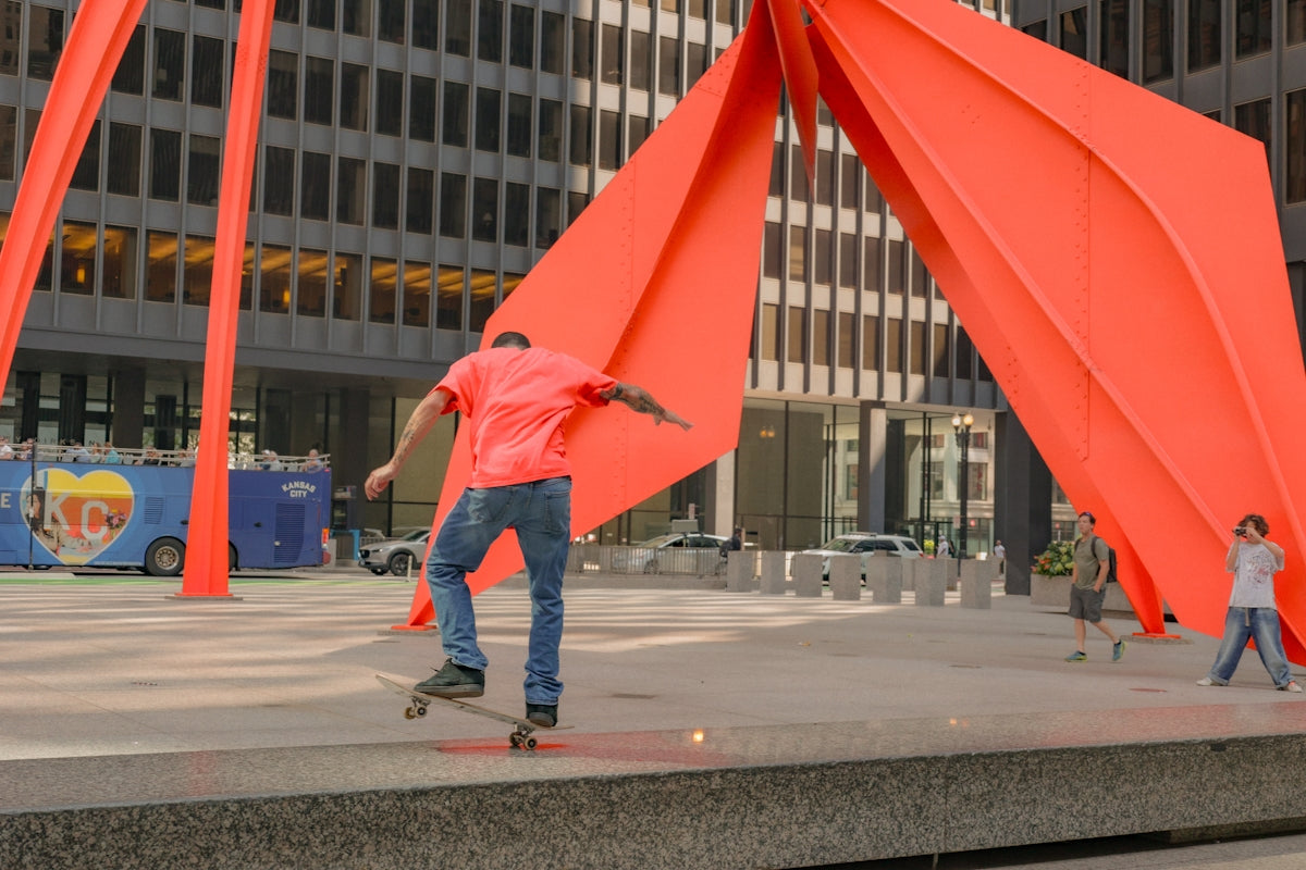 a man riding a skateboard next to a tall orange sculpture