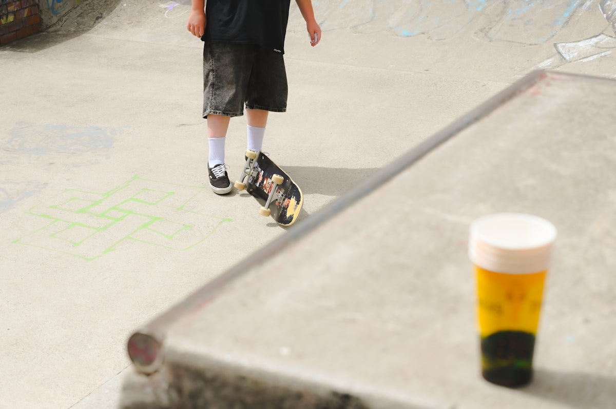 A skateboarder stands near his board and drink.