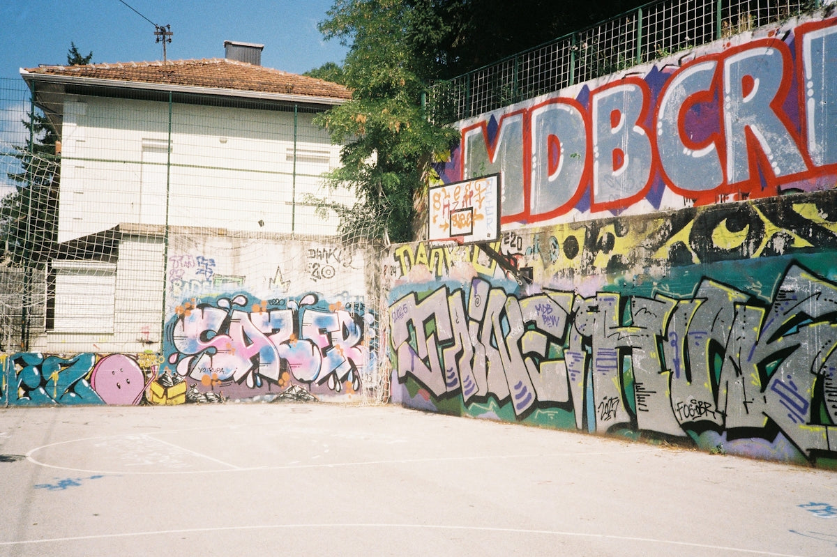 Graffiti-covered walls surround an outdoor basketball court.