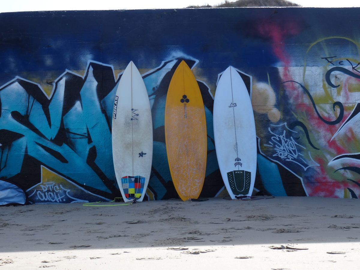 Three surfboards lean against a graffiti wall.